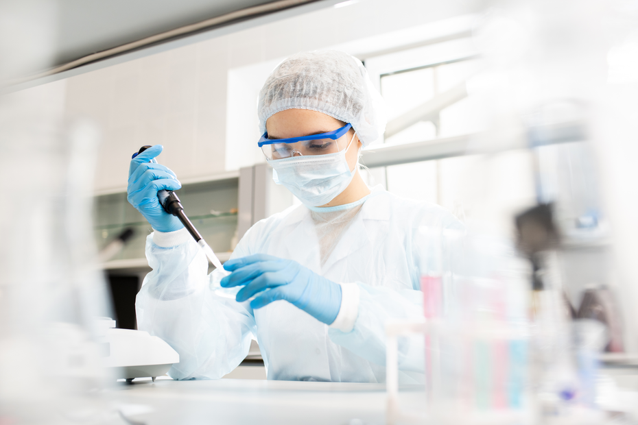 Laboratoriya sharoitida quyoshda ishlovchi kimyo mutaxassisi, pipetka bilan namuna olib, tajriba o'tkazmoqda. U himoya kiyimida, ko'zoynak va niqobda. Orqa fon hareketli, laboratoriya asboblari ko'rinadi.